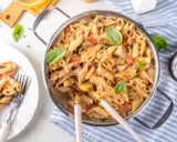 Penne z kremowym sosem, kawałkami suszonych pomidorów i świeżą bazylią. Danie wygląda apetycznie i jest gotowe do podania.