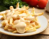 Chrupiące frytki z airfryer polane kremowym sosem serowym. Idealna przekąska, która rozpływa się w ustach.