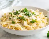 Pyszny makaron z pieczarkami w kremowym sosie, posypany świeżą natką pietruszki i parmezanem. Idealny na szybki obiad.