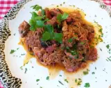 Pyszny bigos z kiszonej kapusty z kawałkami mięsa i kiełbasy, udekorowany natką pietruszki.