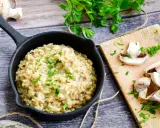 Kremowe risotto z warzywami, posypane natką pietruszki, obok świeże pieczarki na desce.