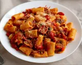 Pyszny makaron z sosem pomidorowym, grzybami i parmezanem na białym talerzu.