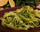 Tagliatelle z aromatycznym pesto z rukoli, podane na brązowym talerzu, z cytryną i orzechami w tle.