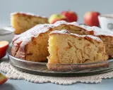 Puszyste, szybkie ciasto z jabłkami, posypane cukrem pudrem, na szklanej paterze. Obok jabłka i filiżanka kawy.