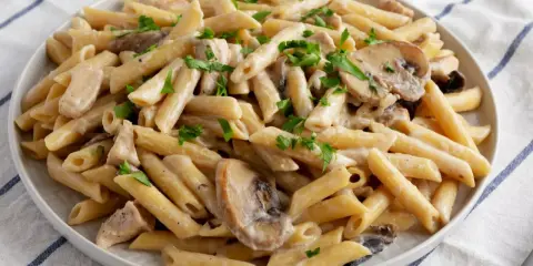 Penne z kurczakiem i pieczarkami w kremowym sosie, posypane natką pietruszki. Pyszne danie makaronowe.