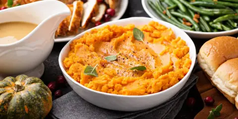 Aksamitne puree z batata, ozdobione listkami ziół, stanowi centralny punkt świątecznego stołu. Obok pieczony indyk, fasolka szparagowa i bułeczki.