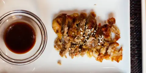 Kawałki chrupiącej kaczki posypane sezamem, obok miseczka z ciemnym, aromatycznym sosem słodko kwaśnym.