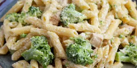 Penne z kurczakiem i kremowym sosem, w którym dominują zielone różyczki brokułów. Danie posypane startym parmezanem.