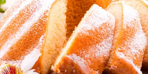 Szybka babka wilgotna, oprószona cukrem pudrem, z widocznymi kawałkami ciasta i ozdobiona kwiatem.
