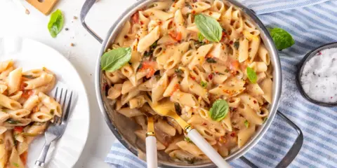 Penne z kremowym sosem, kawałkami suszonych pomidorów i świeżą bazylią. Danie wygląda apetycznie i jest gotowe do podania.