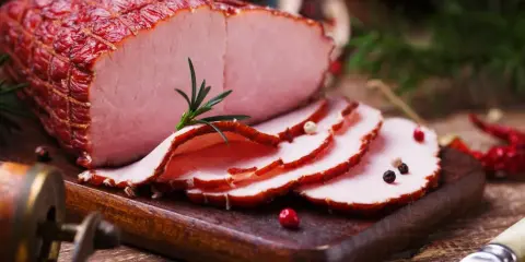 Soczysta szynka gotowana w herbacie, pokrojona w plastry, ozdobiona rozmarynem i pieprzem. Idealna na świąteczny stół.