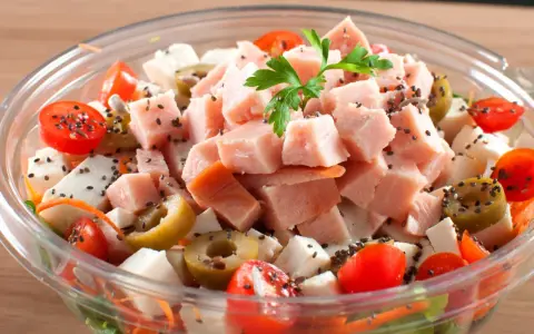 Pyszna sałatka z wędzonym kurczakiem, pomidorkami koktajlowymi, oliwkami i serem feta, posypana czarnuszką.