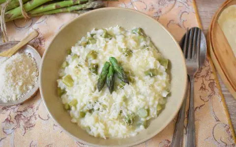 Kremowe risotto ze szparagami, posypane parmezanem, z kilkoma zielonymi szparagami na wierzchu.
