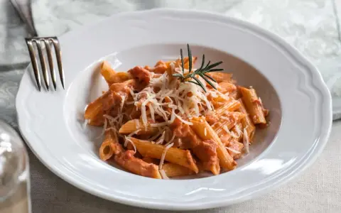 Penne alla vodka z kremowym sosem pomidorowym, posypane parmezanem i udekorowane gałązką rozmarynu.