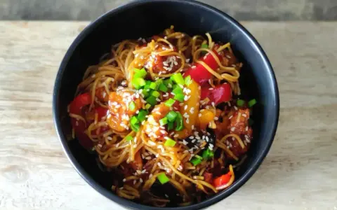 Pyszny makaron chow mein z kurczakiem, papryką i szczypiorkiem, posypany sezamem.