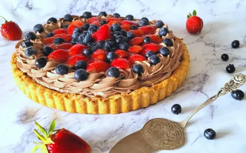 Pyszna tarta z owocami: kruchy spód, czekoladowy krem i świeże truskawki z borówkami. Idealna na deser!