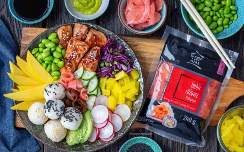 Kolorowy bowl z lososiem, ryżowymi kulkami, mango, awokado, edamame i marynowanym imbirem. Obok opakowanie różowego imbiru.