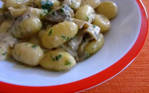 Pyszne gnocchi z sosem grzybowym i natką pietruszki, podane w białej misce z pomarańczowym rantem.