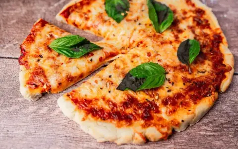 Pyszna pizza z air fryera, z ciągnącym się serem i świeżą bazylią, wygląda apetycznie na drewnianym blacie.