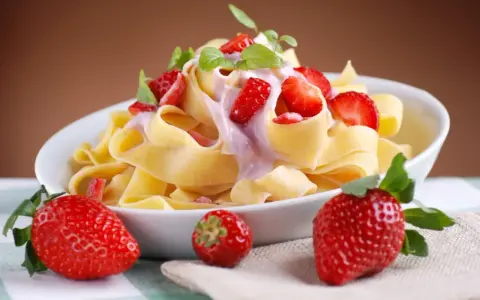 Pappardelle z kremowym sosem i świeżymi truskawkami, ozdobione listkami mięty. Letnia uczta z makaronem i truskawkami.