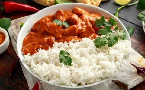 Aksamitny kurczak tikka masala w kremowym sosie, podany z puszystym ryżem i świeżą kolendrą.