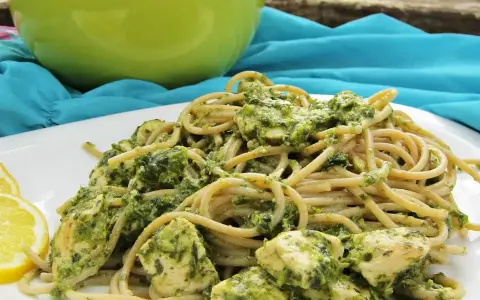 Pyszny makaron z pesto i kurczakiem, podany z plasterkami cytryny.