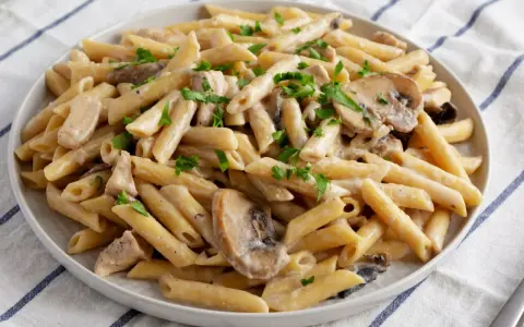 Penne z kurczakiem i pieczarkami w kremowym sosie, posypane natką pietruszki. Pyszne danie makaronowe.