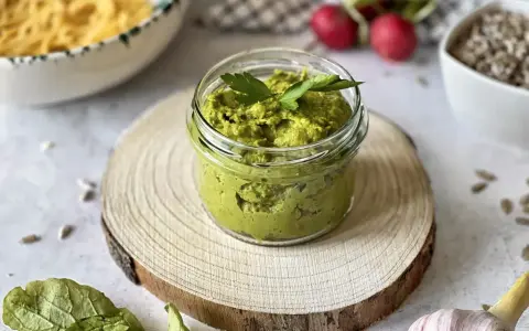 Pesto z liści rzodkiewki w słoiczku, ozdobione natką pietruszki. Obok makaron, rzodkiewki i czosnek.
