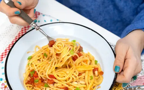 Pyszny obiad bez mięsa: spaghetti z pomidorami, fasolką i szczypiorkiem na talerzu.