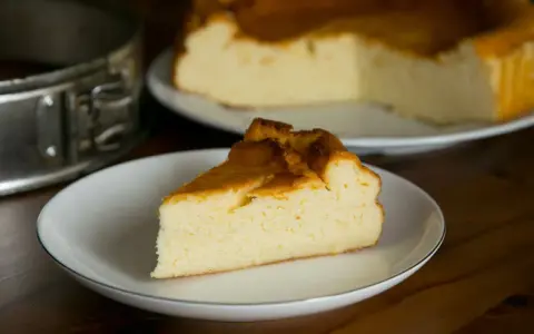 Puszysty sernik z mlekiem skondensowanym, z lekko zarumienioną skórką, na talerzyku. Obok forma do pieczenia.