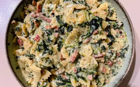 Pyszny makaron farfalle w kremowym sosie ze szpinakiem i kawałkami boczku.