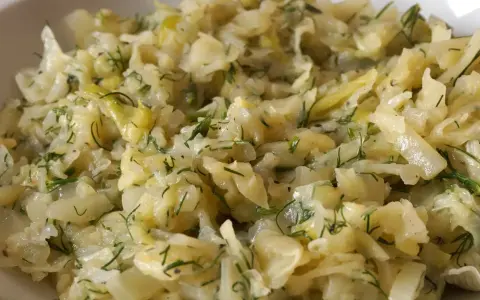 Młoda kapusta zasmażana z koperkiem, podana w białej misce. Danie wygląda na delikatne i aromatyczne.