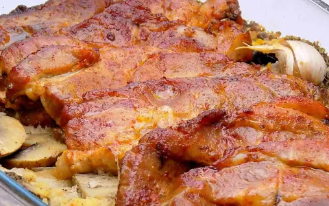 Soczysta karkówka z pieczarkami i ziemniakami, zapieczona w szklanym naczyniu. Aromatyczny czosnek dodaje głębi smaku.