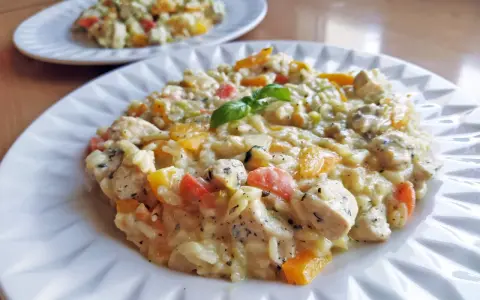 Pyszne risotto z kurczakiem i kolorowymi warzywami, udekorowane listkiem bazylii. Idealne na obiad.