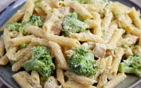 Penne z kurczakiem i kremowym sosem, w którym dominują zielone różyczki brokułów. Danie posypane startym parmezanem.