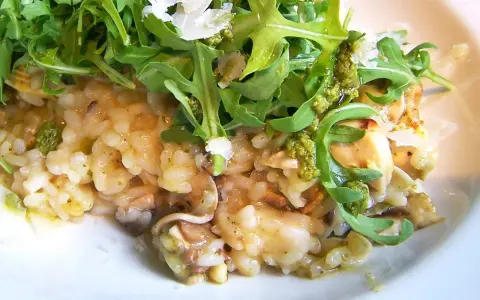 Kremowe risotto z pieczarkami, polane zielonym pesto i posypane parmezanem, udekorowane świeżą rukolą.