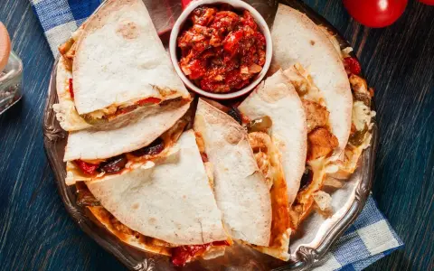 Pyszna quesadilla z kurczakiem, podana z salsą pomidorową na srebrnej tacy. Idealna na szybki posiłek.