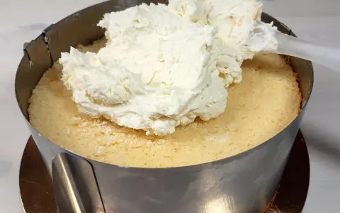 Nakładanie puszystego kremu z mascarpone na biszkopt w tortownicy.