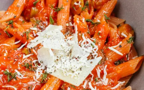 Penne w sosie pomidorowym z oliwkami i parmezanem. Idealny szybki obiad z makaronem, doprawiony ziołami.