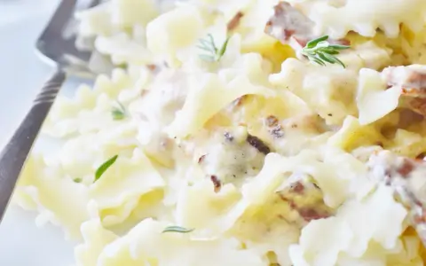 Pyszny makaron farfalle w kremowym sosie śmietanowym z kawałkami boczku i świeżym rozmarynem.