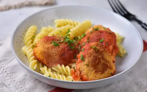 Elegancki obiad dla gości: pulpeciki w sosie pomidorowym z makaronem fusilli, posypane natką pietruszki.