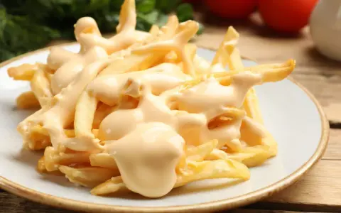 Chrupiące frytki z airfryer polane kremowym sosem serowym. Idealna przekąska, która rozpływa się w ustach.