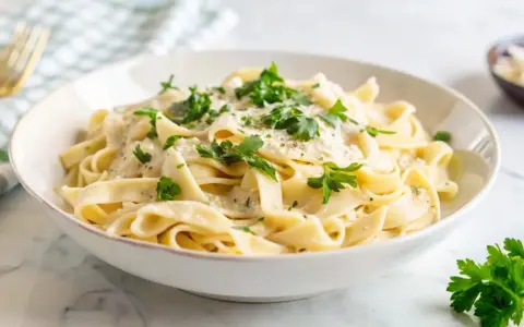 Pyszny makaron z pieczarkami w kremowym sosie, posypany świeżą natką pietruszki i parmezanem. Idealny na szybki obiad.