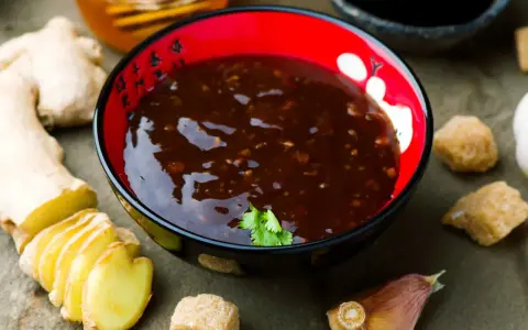 Miseczka z sosem teriyaki, obok świeży imbir, czosnek i cukier. Idealne składniki do przygotowania domowego sosu teriyaki.