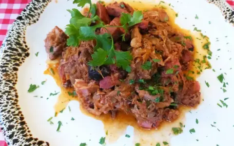 Pyszny bigos z kiszonej kapusty z kawałkami mięsa i kiełbasy, udekorowany natką pietruszki.
