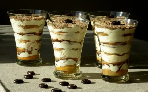Pyszne tiramisu w pucharkach, warstwowo ułożone z kremem i biszkoptami, posypane czekoladą i kawą.