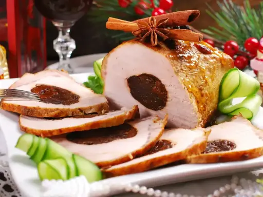 Pyszny schab ze śliwką, pieczony z przyprawami, podany z ogórkiem i dekoracjami świątecznymi.