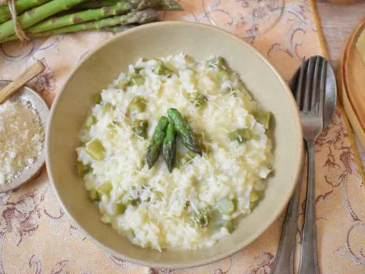Kremowe risotto ze szparagami, posypane parmezanem, z kilkoma zielonymi szparagami na wierzchu.