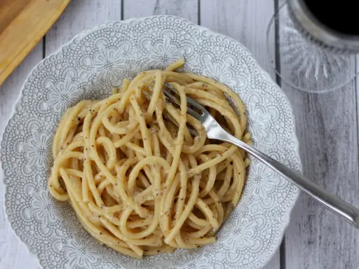 Porcja pysznego cacio e pepe z widelcem w talerzu, gotowa do zjedzenia.