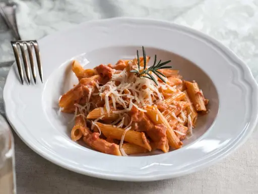 Penne alla vodka z kremowym sosem pomidorowym, posypane parmezanem i udekorowane gałązką rozmarynu.